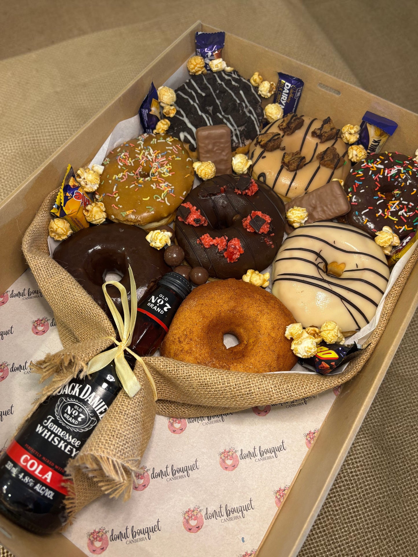 Donut Bouquet Canberra gift box featuring assorted glazed donuts, chocolate bars, popcorn, and a Jack Daniels and Coke bottle.