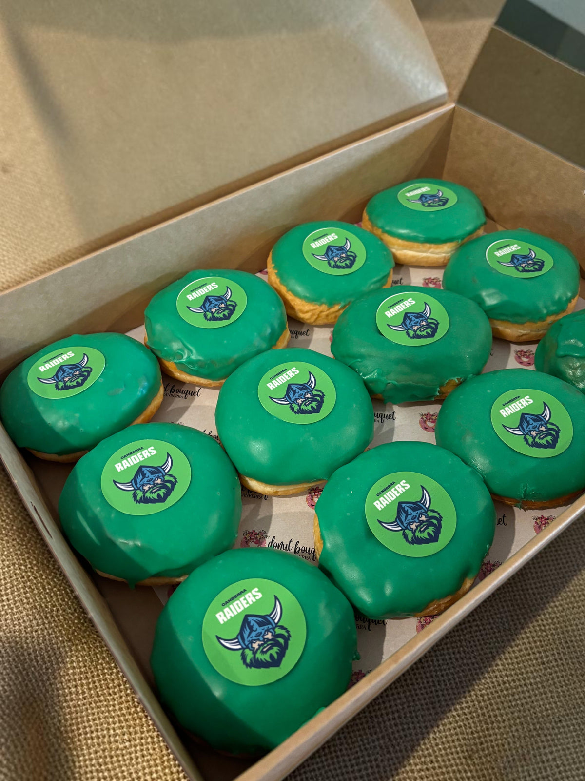 Donut Bouquet Canberra green glazed donuts arranged in rows inside cardboard boxes for a Raiders themed celebration.