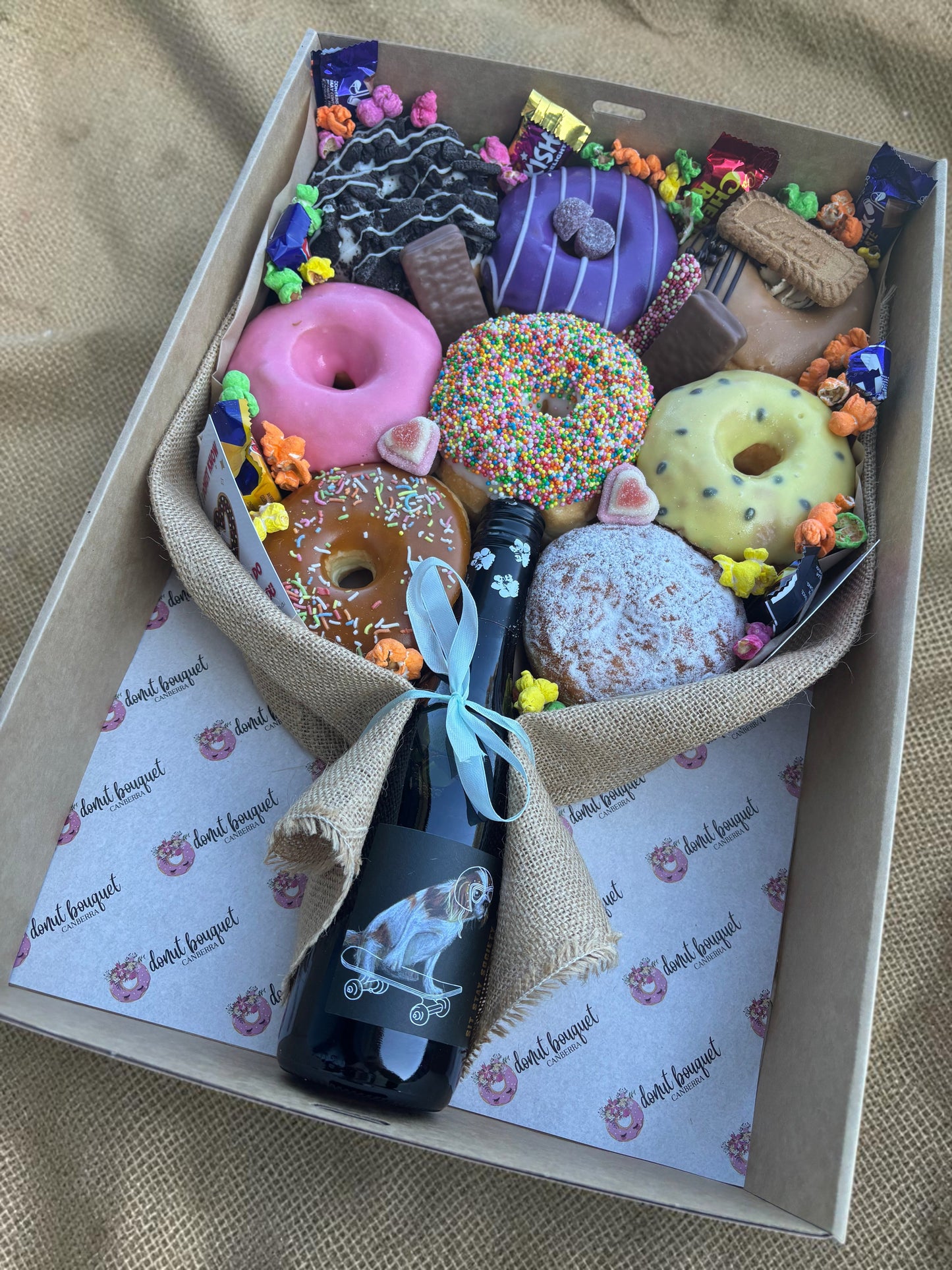Donut Bouquet Canberra gift hamper featuring eight assorted glazed donuts, chocolates, and a central bottle of wine.